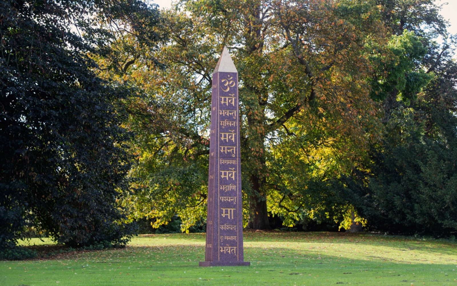 Sanskrit obelisk with gold Om inscription, standing on a lawn among autumn trees