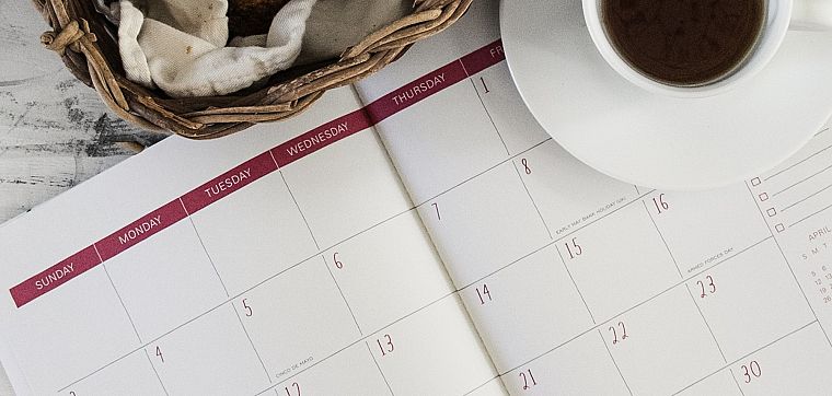An open monthly wall calendar beside a cup of coffee