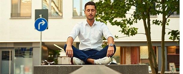 A man sitting cross-legged and still on a low wall in a busy street