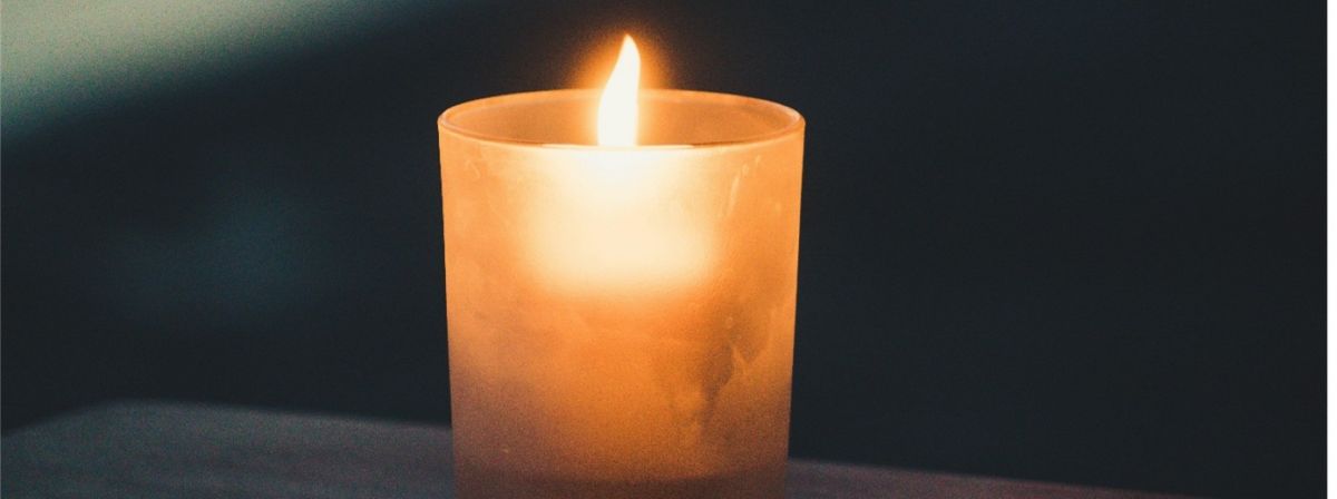 A single lit candle in a frosted glass holder against a dark background